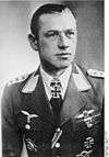 A man wearing a military uniform with various military decorations including an Iron Cross displayed at the front of his uniform collar.