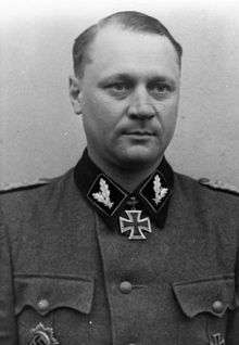 A man in semi profile wearing a military uniform and neck order, in the shape of a cross. His hair is combed to the back.