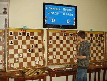 A man looks at three large chessboards on a wall with different positions