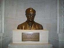 A shining bronze bust of an expressionless man sitting on a pedestal.