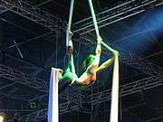 A performer hangs, back arched, between two sheets of tensile fabric.