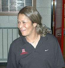 A woman looking to her right. She is wearing a grey polo inscribed with the Nike and Rutgers logos.