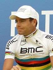 A man in his mid thirties, wearing a mostly white jersey with rainbow stripes in the middle of it.