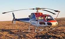A helicopter, painted red at the top, and white at the bottom, is sitting in the middle of a field