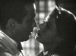 A black-and-white screenshot of a man and woman close together appearing ready to kiss.