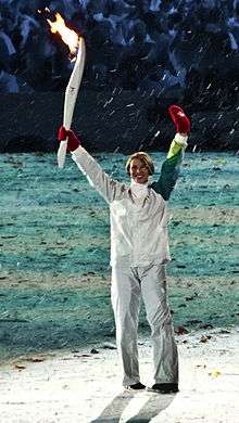 Catriona Le May Doan standing, holding a lit torch in her right hand, waiving to the crowd at the 2010 Winter Olympics opening ceremony.