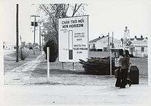 Two women walk past a large sign in Vietnamese and English at an army base