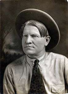 Man with brown hair, shirt with tie, and hat
