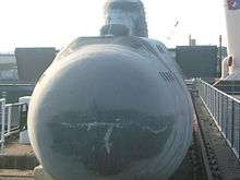 Frontal view of a small submarine in a dockyard.