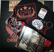 a patch with "GN'R" on it, a keychain, a shirt, a bandana, a sticker all with the same logo and a cd – items from the collector's edition of Chinese Democracy.