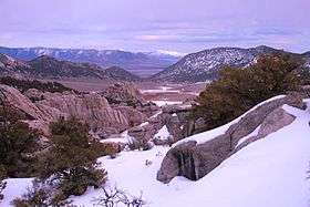 A photo taken from the City of Rocks National Reserve with the Black Pine Mountains in the background and covered in snow