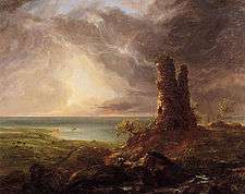 An oil painting showing a ruined stone tower on high ground in the foreground. In the rear is a coast. The sun shines through dark clouds in the sky above.