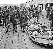Armed soldiers march past a collapsed boat filled with equipment