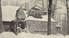  Sepia image of a small snow-covered stone cottage surrounded by tall trees