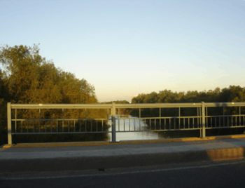 A medium-sized river seen from a bridge with a metal railing.
