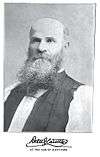 Bald man in white shirt and dark vest, with beard