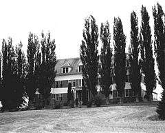 Photograph of the De Smet mission school, a broad, three-story structure situated behind a row of poplars