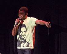 Donald Glover standing onstage holding a microphone and wearing a t-shirt of Alfonso Ribeiro
