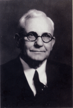 Black and white portrait photograph of an old man wearing glasses.