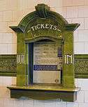 An elaborate ticket office window, tiled in green terracotta, with the word "TICKETS" above the window and "OUT" and "IN" on the left and right sides