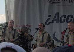 Three aged men dressed with a yellow stripes shirt singing to a microphone.