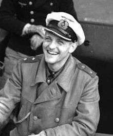 Topp is seen on board, wearing his greatcoat. He is smiling broadly.