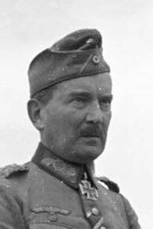 A man with mustache wearing a side cap and military uniform with an Iron Cross displayed at the front of his uniform collar.