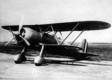 A black and white photograph of a single-propeller biplane on the ground