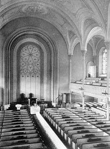 A black-and-white image of a church interior, seen from the gallery. The gallery and vaulted ceiling are supported by small columns.