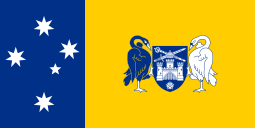 Left third: White stars of the Southern Cross on blue field.  Right two-thirds; black and white swans holding a blue shield with a white castle above a white flower and below a sword and scepter arranged in an "X" formation with a white crown superimposed, all on a yellow field.