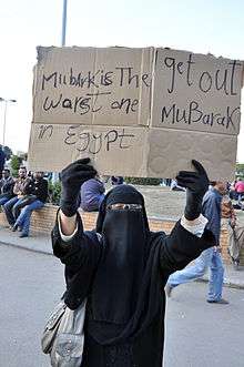 Woman covered in black except for her eyes, holding a sign