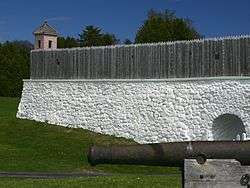 A historic fort, with a wooden fence over a white stone wall that encircles the fort.Fort Mackinac in 2004