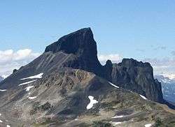 Craggy mountain with its main summit surrounded by a ridge to its right and its left flank covered with rubble.
