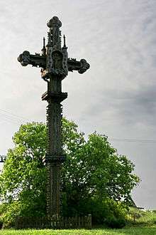 A Lithuanian cross standing by a forest.