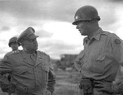 A tall man in military uniform converses with a shorter man in uniform