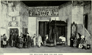 A tall stage set depicting a large room with medieval pictures, patterns and motifs on the upper parts of the walls. On the left, there is an alcove and two sets of doors. At the back is a tall screen and an elaborate curtained four-poster bed containing a man in sleeping garments and a nightcap. To the right is a tall wooden desk with a religious picture in a Gothic frame sideways, near a short staircase leading up to a balcony door. Seven men (two of them tradesmen), three women and a child, all in medieval garments, are standing or sitting around the room listening to an important-looking man who is reading a document out loud.