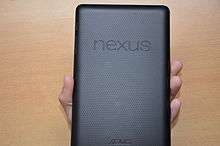 View of the back of a rectangular device held in a hand. The dimpled surface features two prominent words, "Nexus", and "Asus".