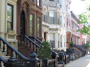 A view down a street with rowhouses in brown, white, and various shades of red.