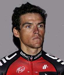 A man in his late twenties, wearing a red, black, and white cycling jersey.