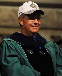 Photograph of Williams wearing a green and black Tulane University graduation gown and a white New Orleans Saints baseball cap