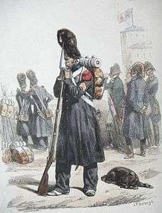 Black and white print of a soldier wearing a bearskin hat, knapsack and a long overcoat. He holds a musket fitted with a bayonet.