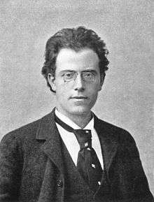 A middle-aged man with glasses and dark hair, wearing a circa-1890s dark suit