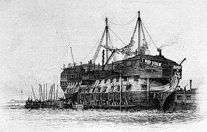 Drawing of the hull of sailing ship without masts, with barred windows, washing strung between poles, a raised superstructure and a barge alongside filled with people.