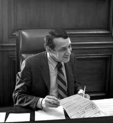 A black and white photograph of Harvey Milk sitting at the mayor's desk