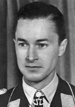 Black-and-white photograph showing the face and shoulders of a young man in uniform. His hair appears dark and is combed to the back. The front of his shirt collar bears an Iron Cross decorations, black with light outline.