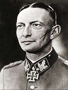A black-and-white photograph of a man in semi profile wearing a military uniform and neck order, in shape of an Iron Cross. His dark hair is combed to the back. He has determined facial expression and a large scar on his cheek.