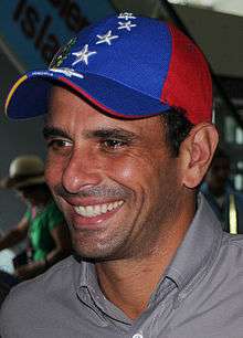A man smiling while wearing a hat with the colours of the Venezuelan flag: red, blue and yellow.