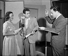 Two men and a woman in radio studio, one man directing the other two