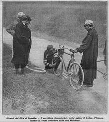 A man working on the front tire of a bicycle; three men are watching.
