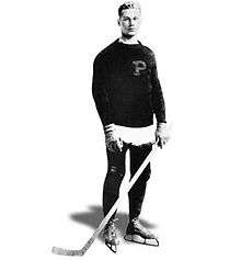 Young man posing for a photo wearing skates and holding a hockey stick. He is also wearing a sweater with a large letter "P" on it
